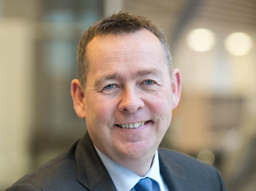 Søren B. Sørensen ser ind i kameraet og smiler. Han er iført jakkesæt.